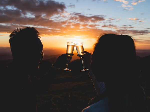 a couple clanking wine glasses amidst a sunset backdrop