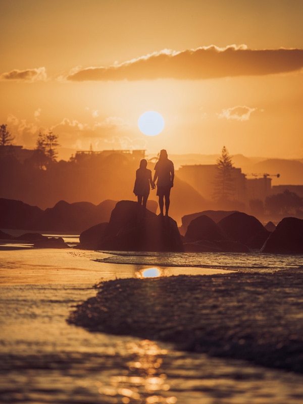 a couple posing against a sunset backdrop at Snapper Rocks