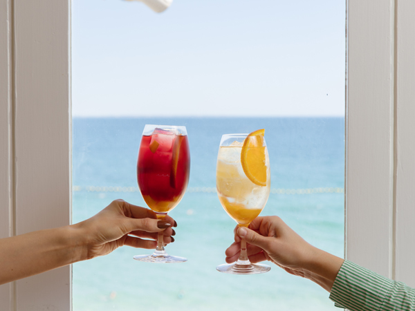 hands raising two cocktail glasses set against the sea view