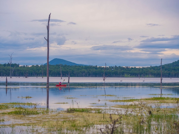 A man in a red kayak on a lake surrounded by trees and mountains.