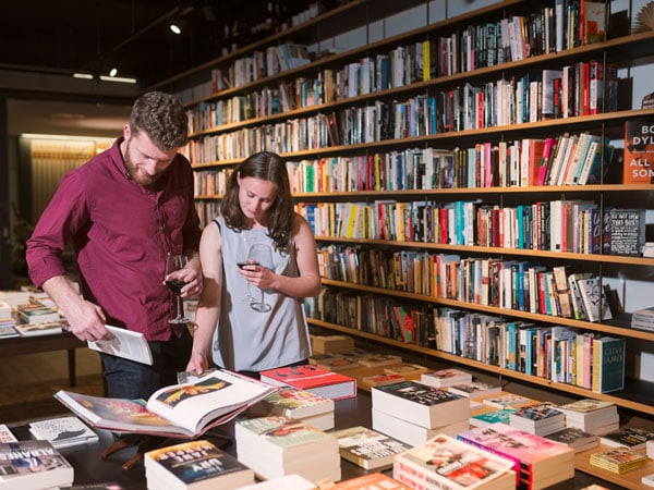 a student couple browsing books with a wine in hand at Muse, Canberra