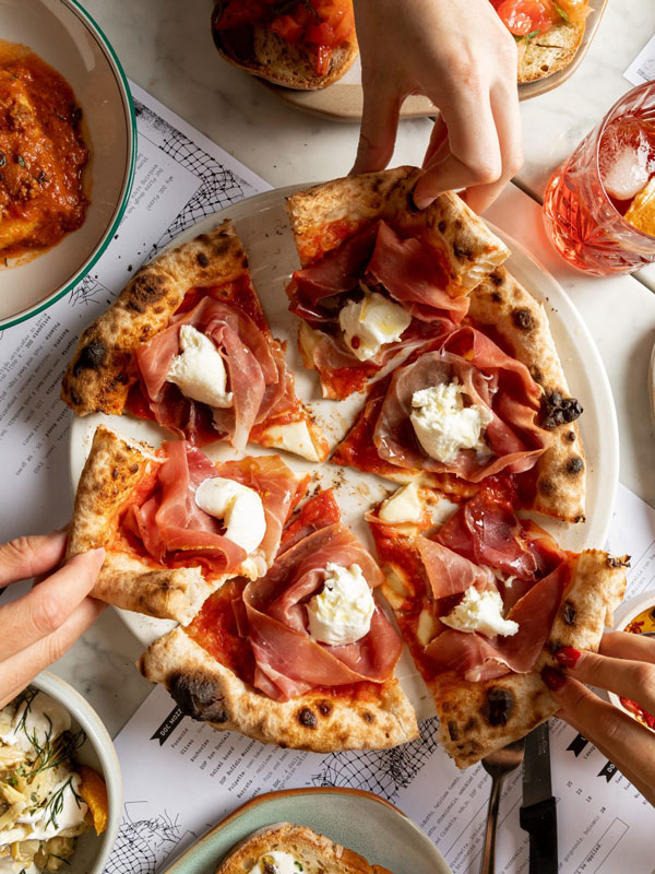 hands getting slices of pizza on the table at D.O.C Pizza & Mozzarella Bar, Carlton