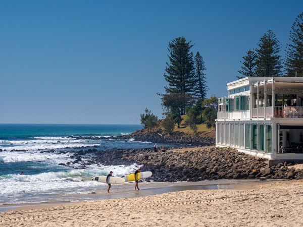 two people strolling along Burleigh Heads beach with their surfboards