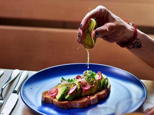 a hand squeezing lemon on avocado toast onboard Virgin Voyages
