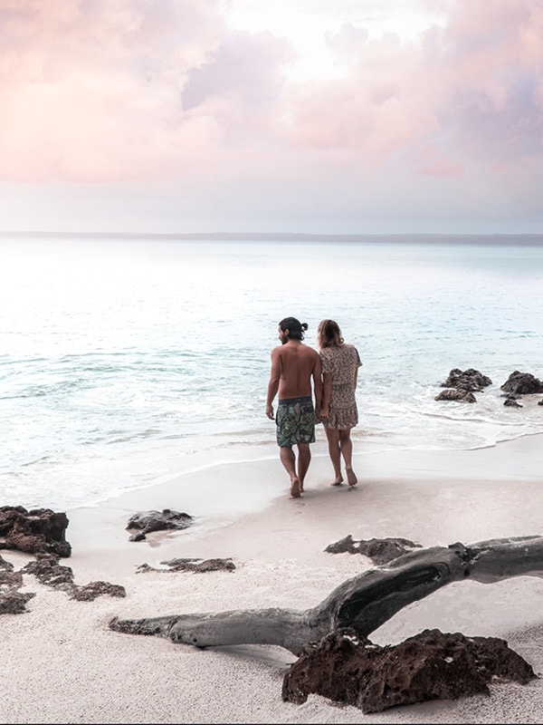 A couple standing a tht edge of the water on a white sand beach