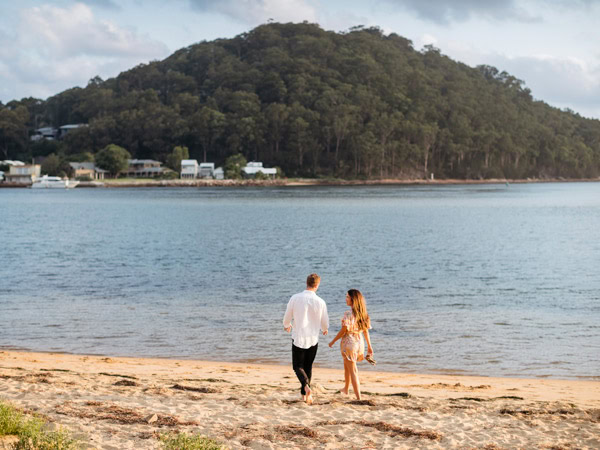 Couple enjoying a walk along Ettalong Beach at sunset.