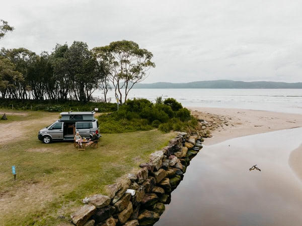 A couple sitting in front of a campervan overlookingUmina Beach, at the NRMA Ocean Beach Holiday Resort in Umina.
