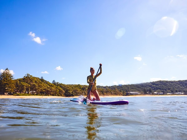 Woman enjoying a morning of stand up paddleboarding atPearl Beach on the Central Coast.