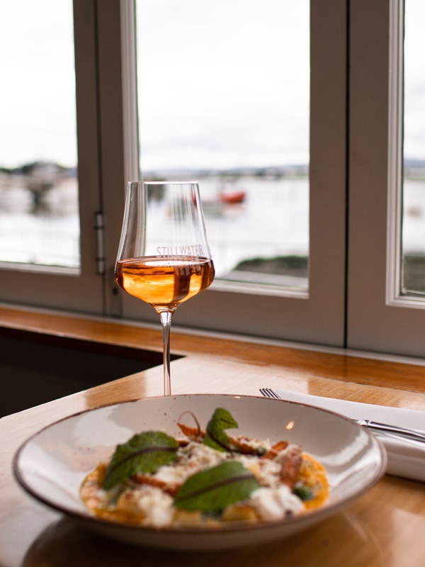 Glass of rose and dish with waterfront views at Stillwater in the background.