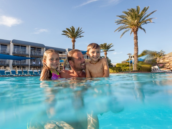 a father with his two children swimming in the pool at Sea World Resort