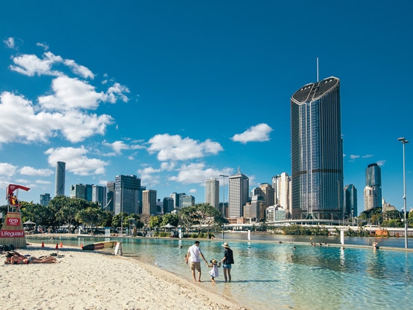 A family walking on the beach and in the water surrounded by buildings.