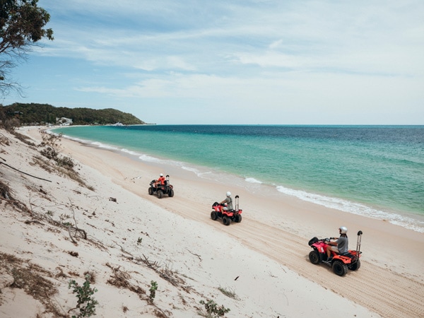 Three people driving quads on a beach.