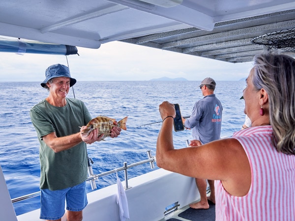 a couple taking photos of a fish they caught, while on a Cairns Reef Fishing tour