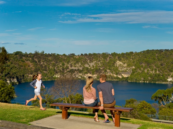a couple sitting on a bench with a young girl jogging on the side of Blue Lake, Mount Gambier