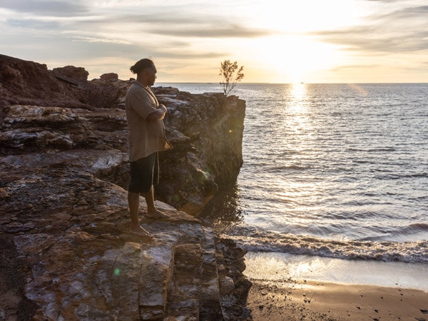 a man standing on top of a beach rock at sunset