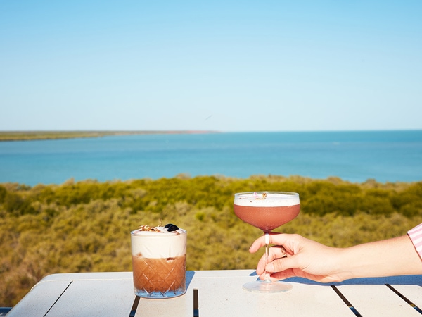 a hand holding a glass of cocktail amid sea views at Mangrove Hotel