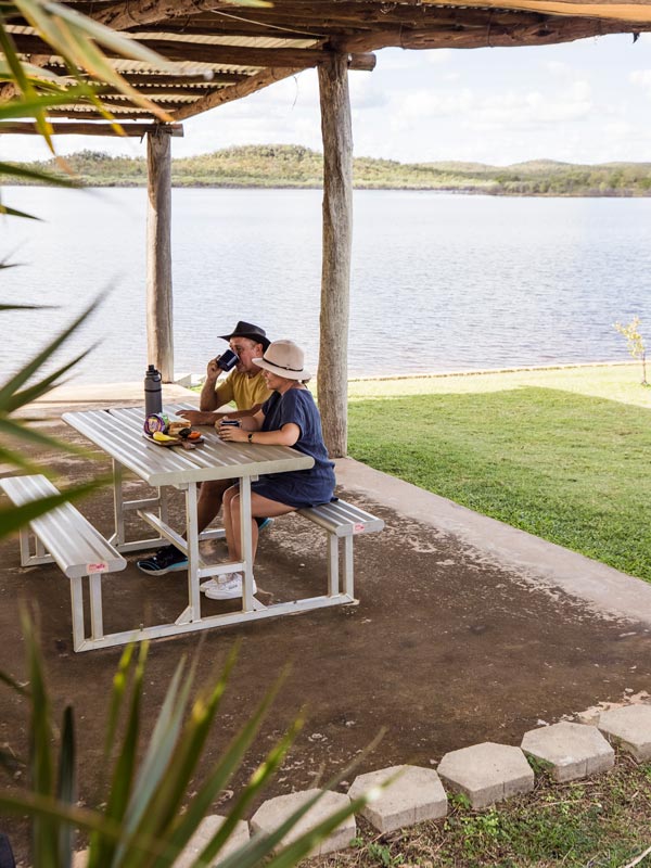 two people eating on a picnic table beside Lake Belmore