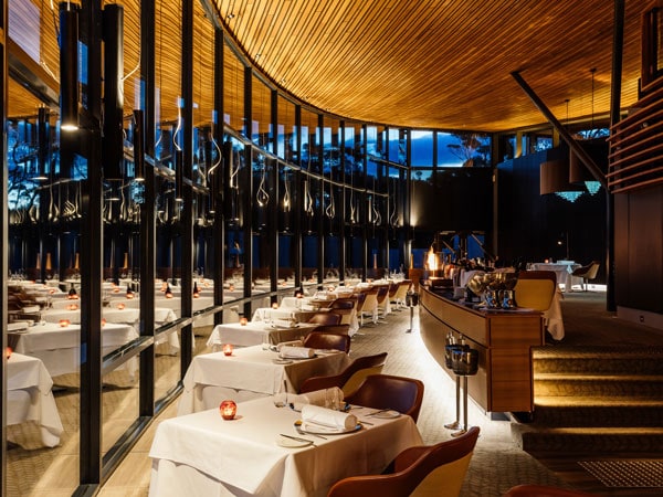 Tables for diners sit by floor to ceiling windows next to a fireplace. (Image: Supplied Courtesy of Saffire Freycinet)