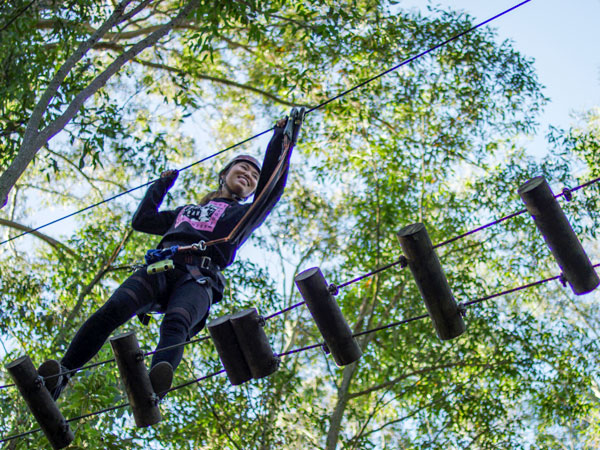 a woman crossing over an elevated obstacle at Treetops Adventure Park, Newcastle