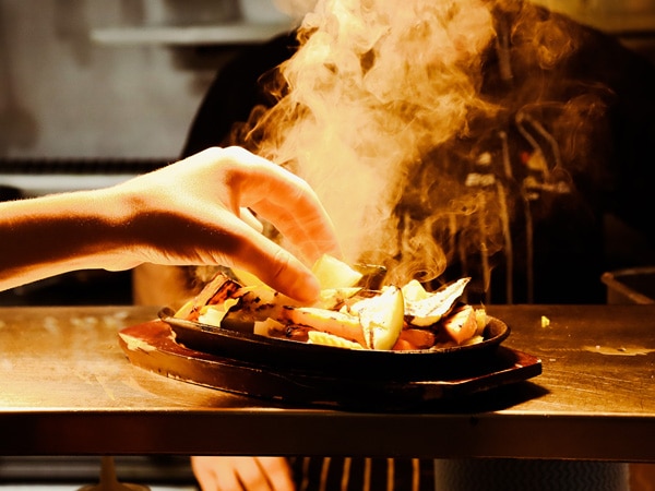 a hand reaching for smoky hot food at El Corazon Cocina de Mexico