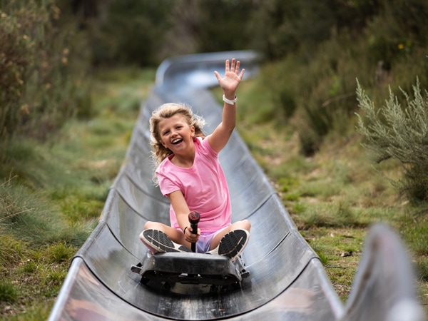 a little girl raising one hand while while zooming down the Alpine Bobsled