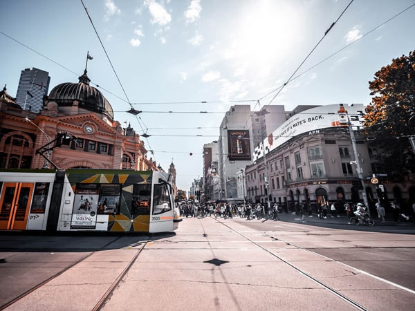 Tram and crowds of Melburnians at a crossroads near Flinders Street Station.