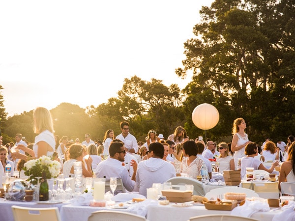 People in white sitting at tables outside and talking.