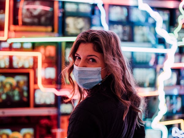 Woman wears face mask in front of neon signs