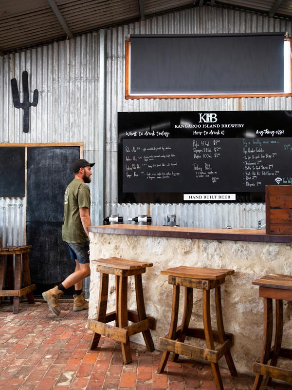 Kangaroo Island Brewery worker walks behind bar with rustic scenery.