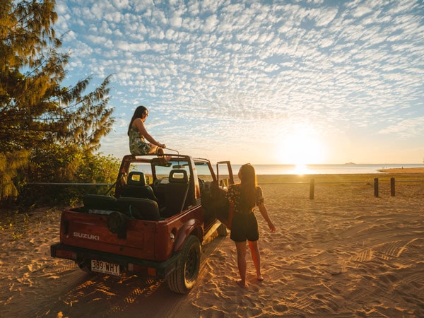 Two girls watch the sunset from their car at West Point, an island town and suburb of Magnetic Island in the city of Townsville, Queensland. (Image: Tourism and Events Queensland)