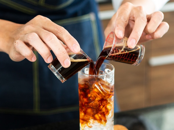 Barista making Ice coffee in a tall glass by pouring brew coffee over ice on a old rustic wooden table. Young barista pouring cold brew coffee into glass on table. The process of pouring fresh brew coffee into a glass.