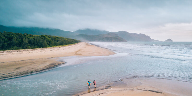 Two people crossing a beach along the Thorsborne Trail