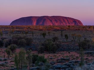 The sun sets over one of the great natural wonders of the world, Uluru towers above the surrounding landscape. (Image: Tourism NT/Che Chorley)