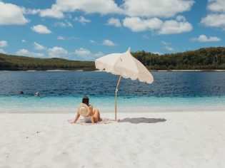 A woman relaxes on the white sand at Lake McKenzie(Image: Tourism and Events Queensland)