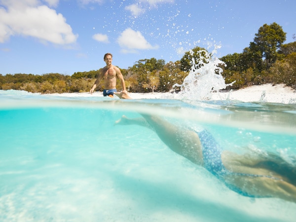 A woman dives into the water at Lake McKenzie with her partner behind her. (Image: Tourism and Events Queensland)