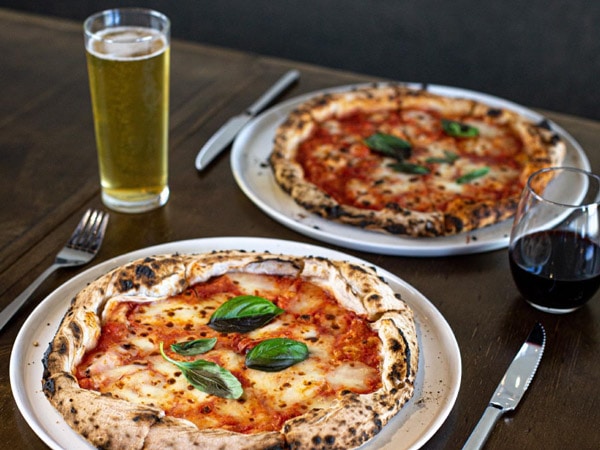 two plates of classic margherita pizza with a glass of beer on the side