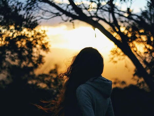 Woman looking at sunset through trees