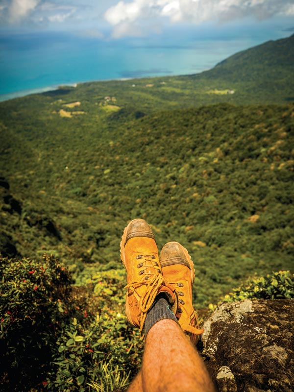 Mans hiking boots with the view from the top of Mount Sorrow in Cape Tribulation. (Image: Tourism Tropical North Queensland)