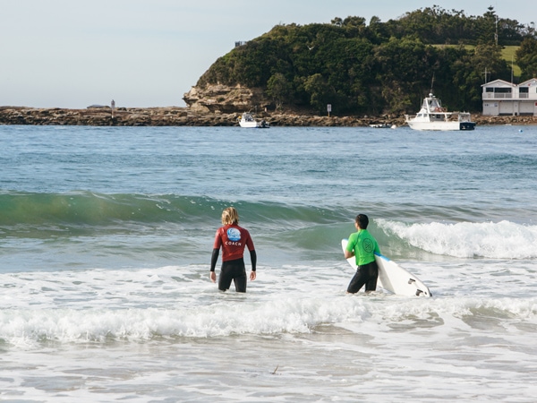 A Central Coast Surf Academy coach and student heading out into the water in Central Coast, Australia