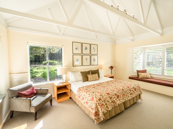 A bedroom with yellow walls, a bed, bedside table and a couch with pillows.