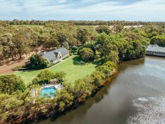 A photo of a white building and a swimming pool surrounded by trees and a river viewed from above.