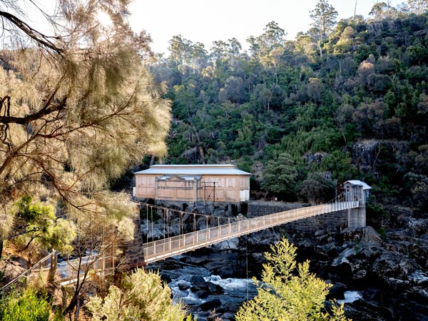 A power station near a bridge suspended over the river and surrounded by trees.