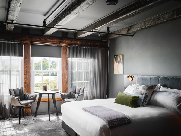 A grey themed bedroom with a bed, table, chairs with pillows, and curtains.