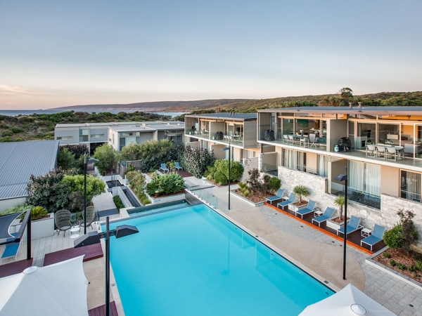 A swimming pool surrounded by a resort in front of the ocean