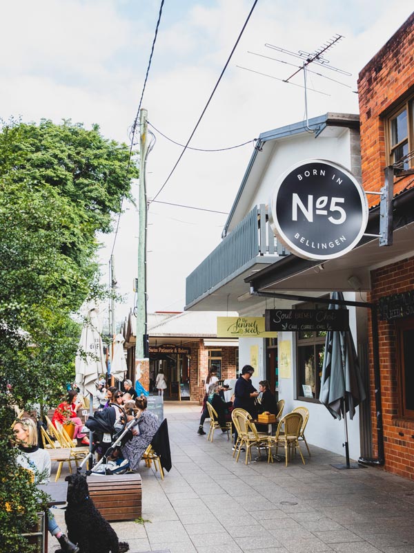 A photo of a street in a town centre with cafes where people are sitting down.