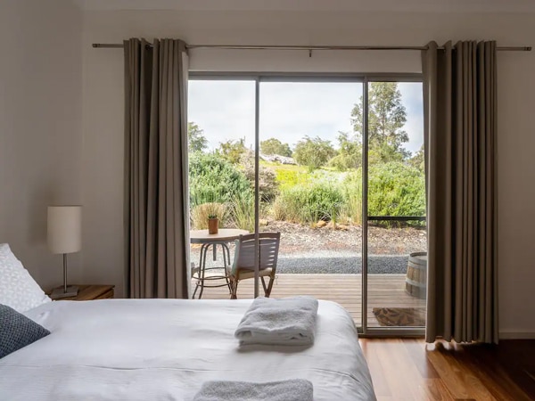 A photo of a bed indoors with towels in a bedroom with curtains and an outdoor space with a chair and a table.