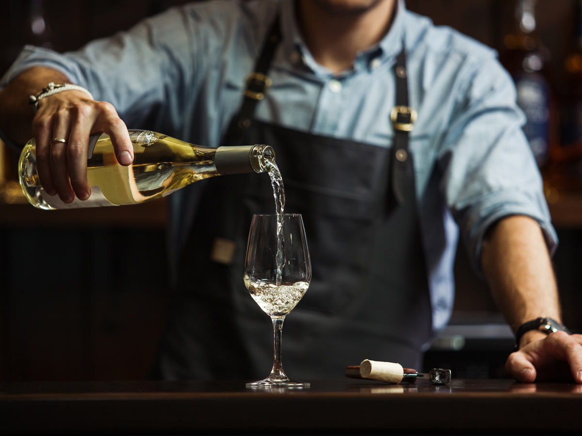 a bartender pouring white wine into a long-stemmed glass