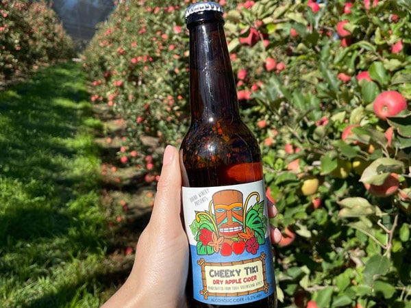 a person holding a bottle of Cherry Tiki Dry Apple Cider behind the apple orchard at Ohana Cider House & Tropical Winery