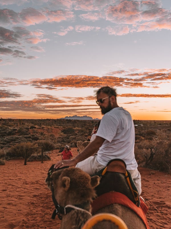 seorang pria menunggang unta sebelum matahari terbenam di Uluru