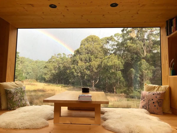 a see-through glass wall with a view of the forest and rainbow at Bruny Island Hideaway